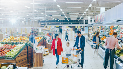 At the Supermarket: Happy Family of Three, Holding Hands, Walks Through Fresh Produce Section of the Store. Father, Mother and Daughter Having Fun Time Shopping. High Angle Panoramic Shot.