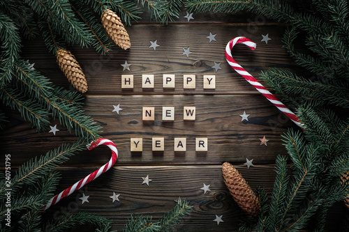 Fotografie, Obraz Happy new year phrase on woodden rustic table surounded with fur tree branches, cones, stars and candy canes
