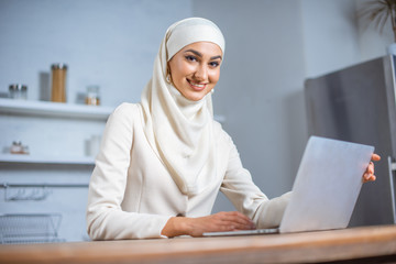 Wall Mural - beautiful young muslim woman using laptop and smiling at camera