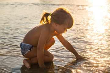 Caucasian blonde little girl playing with sand on the beach at sunset