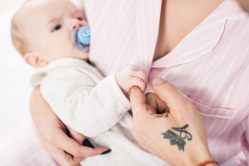 cropped shot of baby holding fathers finger while resting on mothers hands