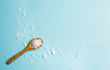Magnesium Chloride Flakes scattered around brown wooden spoon on blue background. For making foot bath, taking a magnesium-rich bath allows full body exposure to a concentrated solution of magnesium.