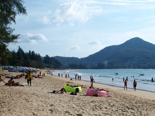 Sunbathing resting swimming people in the beach with sunbeds and sun umbrellas. Panoramic view of paradise resort at the tropical island. Forest and mountain at the background. Summer holiday. 