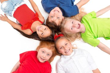 Wall Mural - Close-up of happy children lying on floor in studio and looking up, isolated on white background, top view. Kids emotions and fashion concept