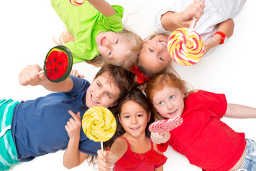 close-up of happy children with candy lying on floor in studio and looking up, isolated on white bac