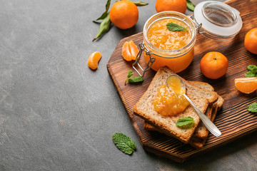 Jar of tasty tangerine jam with toasted bread on grey table