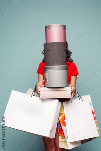 Fotografía Studio portrait of incognito brunette woman in red dress holding at hands many bags, boxes and presents after shopping