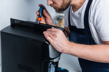 Wall Mural - cropped image of handyman in working overall repairing coffee machine by screwdriver in kitchen