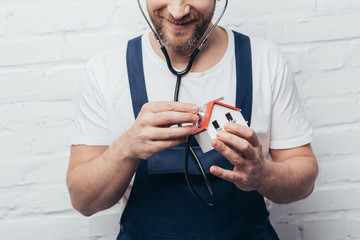 Wall Mural - partial view of male handyman checking house figure by stethoscope, home inspection concept