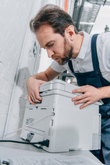 Wall Mural - serious male handyman repairing copy machine in modern office