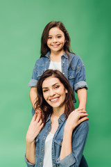 smiling mother and daughter holding hands and looking at camera isolated on green