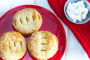 Selection of puff pastry mince pies on a red plate served with a small bowl of fresh cream