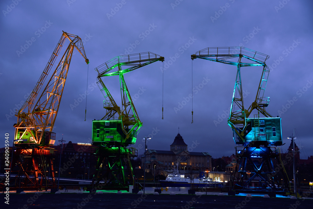 Colorfully illuminated antique cranes on the quay of Szczecin Łasztownia. - obrazy, fototapety, plakaty 