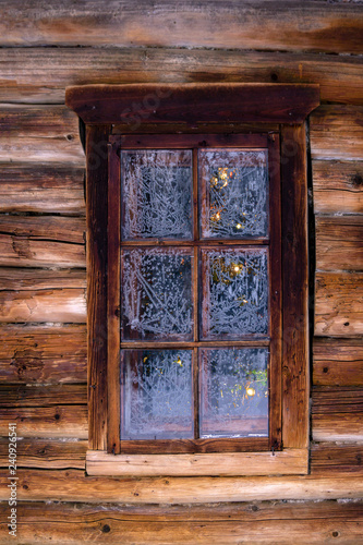 Fotografía Christmas tree behind the window in the log wall of an old building
