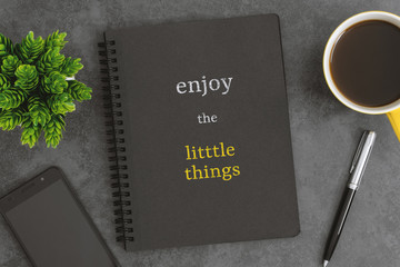 Notebook, mobile phone, pen and coffee cup on dark gray background. Short quote about life.