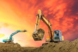 Two excavators work on construction site at sunset
