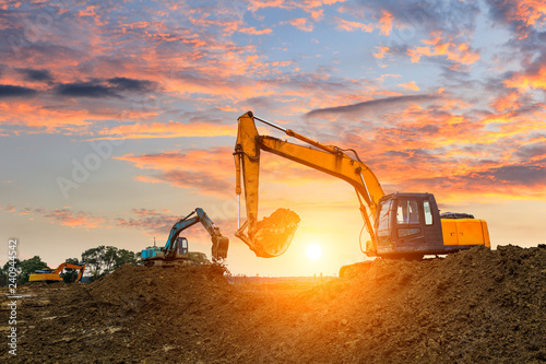 Fotografía Three excavators work on construction site at sunset