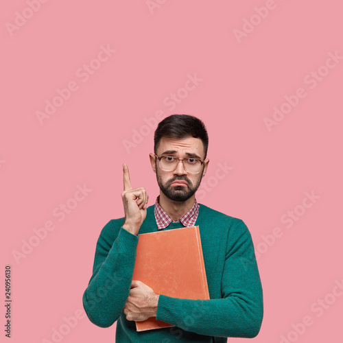Fotografie, Obraz Unhappy displeased guy frowns face, indicates with index finger above, wears spe