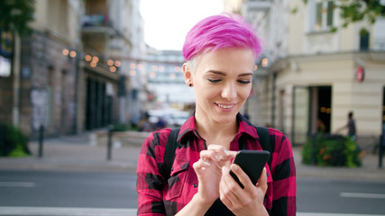 A young woman with a pink short hair using a phone in the city street. Close-up shot. Soft focus