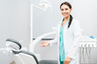 © LIGHTFIELD STUDIOS - smiling female dentist showing chair in dental clinic