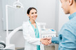 © LIGHTFIELD STUDIOS - smiling female dentist shaking hands with  african american patient