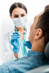 Wall Mural - selective focus of female stomatologist in latex gloves and mask examining african american patient