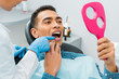 © LIGHTFIELD STUDIOS - female dentist touching tooth of handsome african american man looking at mirror