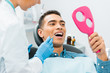 © LIGHTFIELD STUDIOS - female dentist holding medical instrument near african american patient looking at mirror