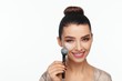 © Andriy Goncharenko - Portrait of a beautiful young woman holding a brush in her hand and applying powder to her face with a brush