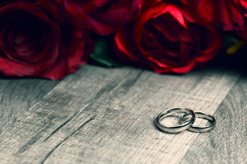 Two engagement rings and red roses flower bouquet with copy space on wooden background. Valentine's Day