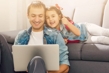 Wall Mural - Bearded man and little girl at home family time sitting on floor on carpet browsing laptop together smiling joyful