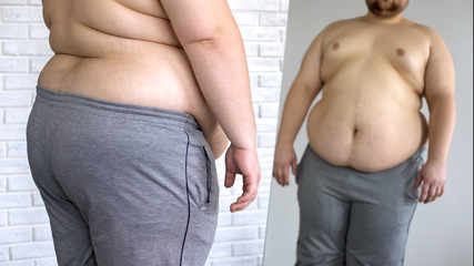 Sad overweight man looking at fat belly mirror reflection, weight loss problem