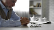Retiree male sitting alone at kitchen table taken off his glasses, poor vision
