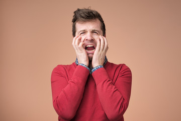Wall Mural - Young european man in red sweater crying of pain anf grief on brown background.