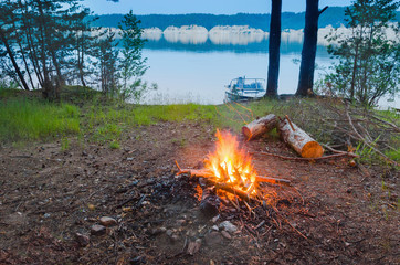 Wall Mural - Big night bonfire at the shore of the river in a forest glade, flames, sparks.