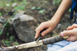 Mano de un niño con navaja quitando corteza rama en bosque