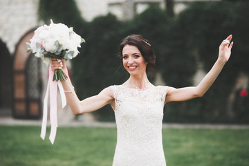 Beautiful brunette bride in elegant white dress holding bouquet posing neat trees