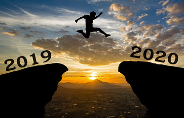 A young man jump between 2019 and 2020 years over the sun and through on the gap of hill  silhouette evening colorful sky. happy new year 2020.