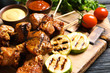 Delicious barbecued meat served with garnish and sauces on wooden board, closeup
