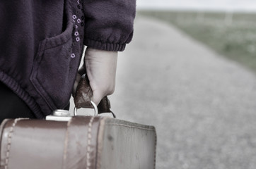 Wall Mural - Refugee girl walking with her old suitcase on the road on the countryside