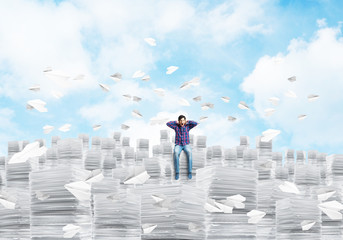 Attractive man sitting on pile of paper documents.