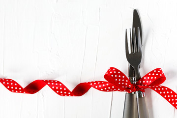 Fork and knife tied with a red ribbon on white background with copy space. Food, restaurant and table setting theme