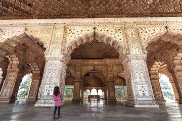 Female tourist at Red Fort Delhi with intricate white marble carvings and interior artwork.