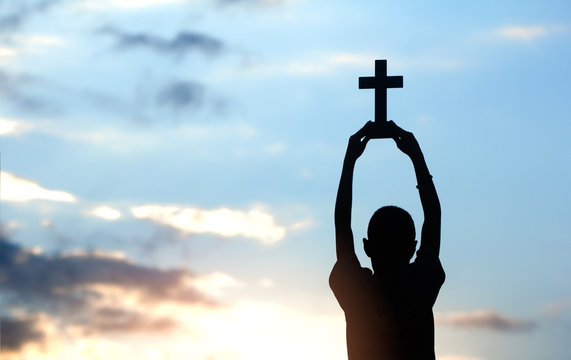 Boy holding christian cross overhead with light sunset background,christian concept.