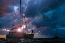 The Dark Silhouette Of Catamarans On Open Sea With Dramatic Clouds During Sunset. The Fisherman Fishing On Bow