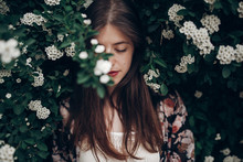 Calm Portrait Of Beautiful Hipster Woman In Blooming Bush With White Flowers Of Spirea. Boho Girl Sensual Portrait In Floral Modern Clothes In Greenery. Space For Text