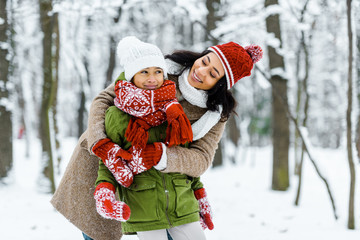 attractive african american mother hugging cute preteen daughter in winter forest