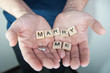 © strigana - Alphabet letter wooden blocks tiles with words Marry me in man hands. Marriage proposal and love concept for Valentine`s day with wedding or engagement ring with brilliant