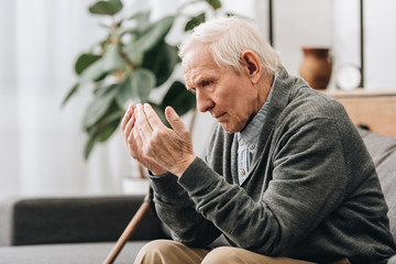 Wall Mural -  pensioner with grey hair looking at hands while sitting on sofa