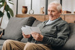© LIGHTFIELD STUDIOS - happy senior man with grey hair lookinf at photos and sitting on sofa